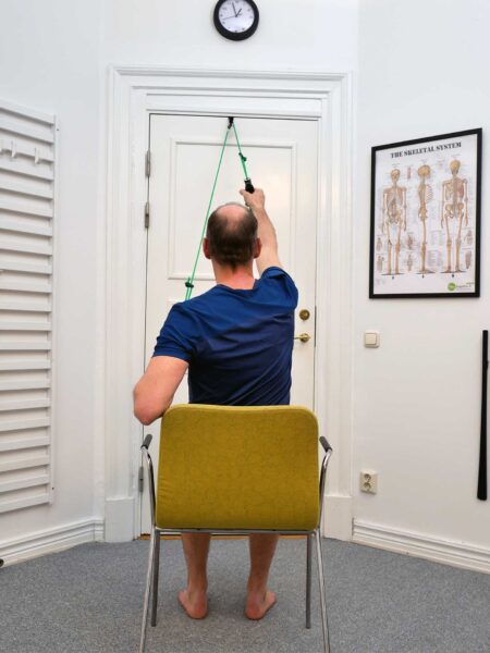 Person sitter på stol framför en dörr och håller en rem i båda händerna.