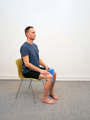 Person sitter på stol med en kudde mellan knäna och fötterna rakt under kroppen.