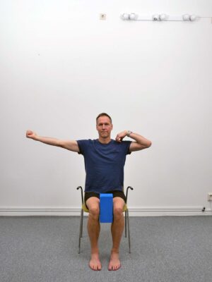 Person sitter upprätt på stol med kudde mellan knäna.