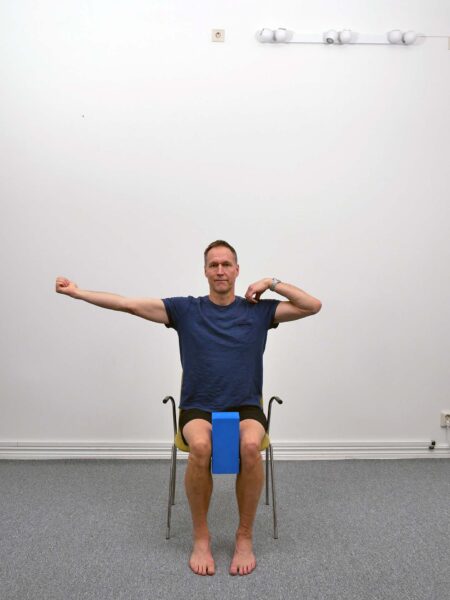 Person sitter upprätt på stol med kudde mellan knäna.