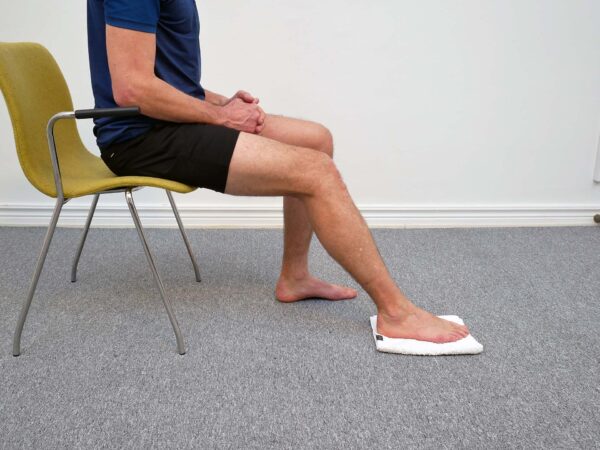Person sitter på stol med foten placerad på handduk på golvet och hälen i kontakt med underlaget.