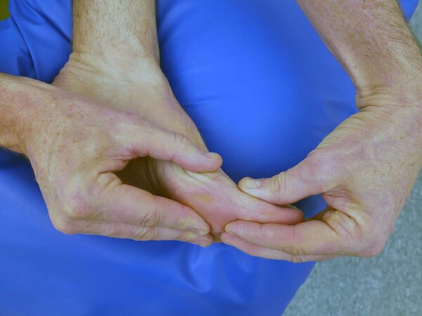 Person sitter på stol med ena foten placerad över motsatt knä och handen vid stortån.