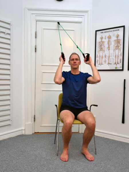 Startposition: Person sitter på stol vid dörr och håller slynga med båda händerna i startläge.