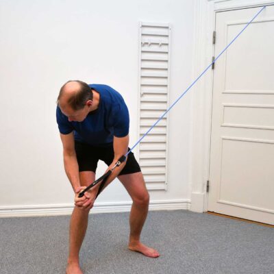 Person har dragit gummibandet diagonalt ned mot motsatt ben med kontrollerad rotation och lätt framåtfällning.