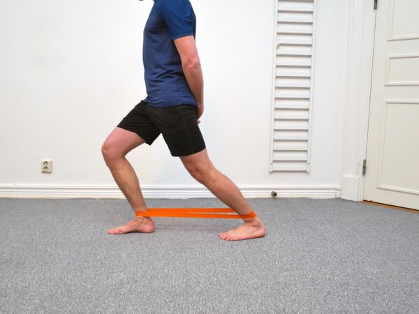 Person står med knät tydligt framfört över foten i maximal dorsalflexion med hälen stabilt i underlaget.