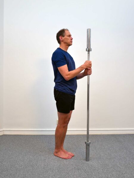 Person står upprätt och håller en skivstång vertikalt framför kroppen med båda händerna.