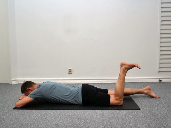 Person ligger på mage med ena knät böjt cirka 90 grader och pannan vilande på underarmarna.