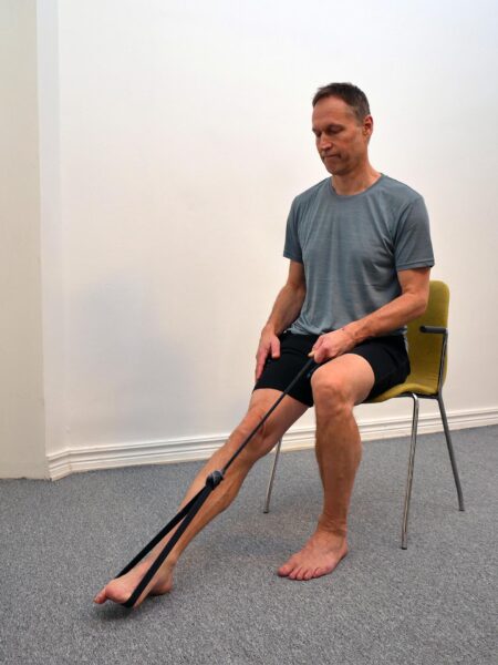 Person pressar foten framåt i plantarflexion mot gummibandets motstånd.