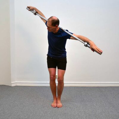 Person har roterat överkroppen maximalt åt sidan med skivstången över axlarna.