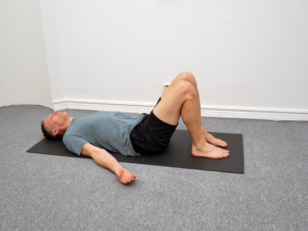 Person ligger på rygg med böjda ben och ena foten placerad över motsatt knä.