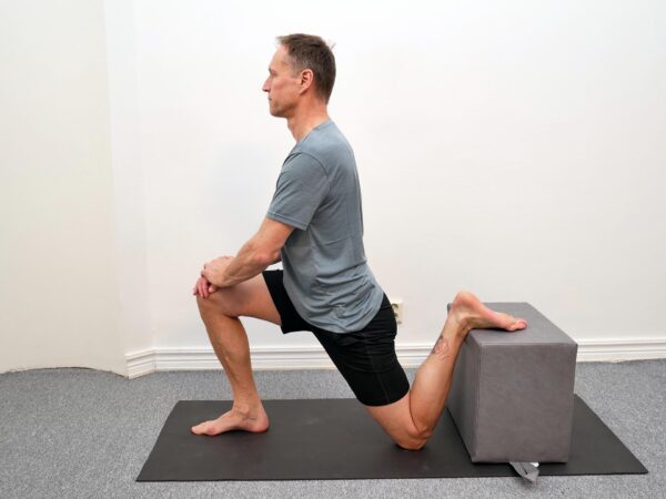 Person i knästående med ena foten placerad på stol bakom kroppen.