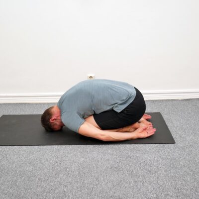 Person sitter på knä med överkroppen vilande framåt över låren.