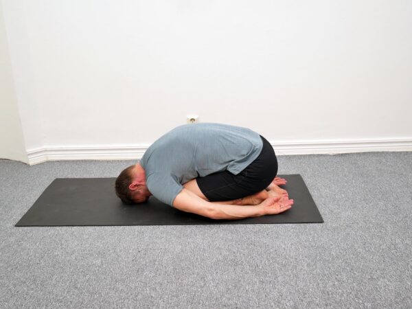 Person sitter på knä med överkroppen vilande framåt över låren.