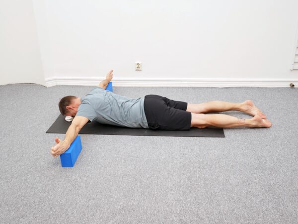 Person ligger på mage med armarna placerade på kuddar med armarna rakt ut åt sidan och pannan mot underlaget.