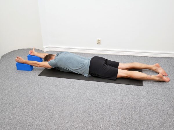 Person ligger på mage med armarna placerade på kuddar och pannan mot underlaget.