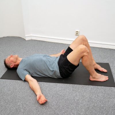 Person ligger på rygg med böjda knän och fötterna i golvet. Bäckenet rörs i en kontrollerad cirkulär rörelse med stabil överkropp.