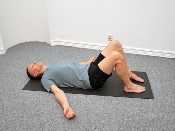 Person ligger på rygg med böjda knän och fötterna i golvet. Bäckenet rörs i en kontrollerad cirkulär rörelse med stabil överkropp.