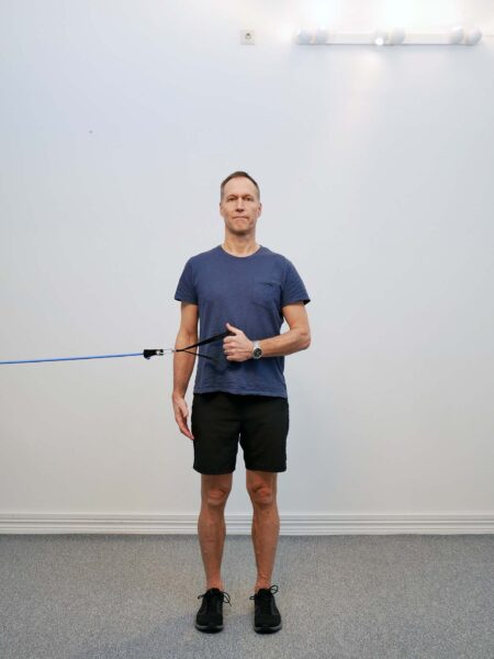 Person står med armbågen intill kroppen och håller ett gummiband.