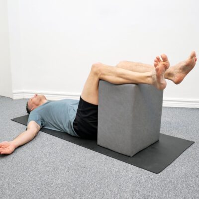 Person ligger på rygg med benen vilande på stol i 90 graders vinkel.