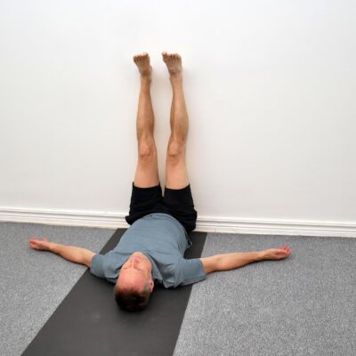 Person ligger på rygg med benen upp mot en vägg och armarna avslappnade vid sidan.