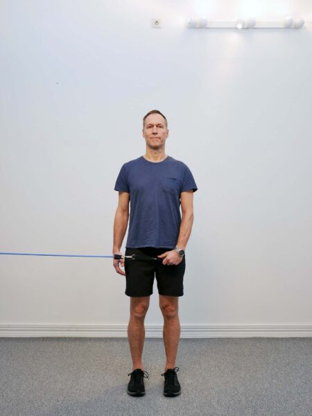 Stående med gummiband i hand vid midjan i utgångsläge för axel-abduktion med tummen ned empty can