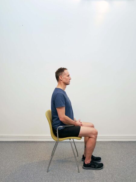 Sittande på stol med huvudet i normalt framåtskjutet utgångsläge - startposition för nack-retraktion chin tuck