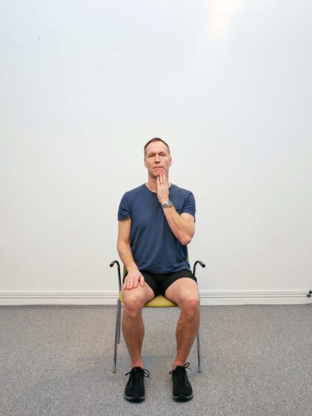 Sittande på stol med huvudet vridet åt sidan inför hand-assist med övertryck i nack-rotation